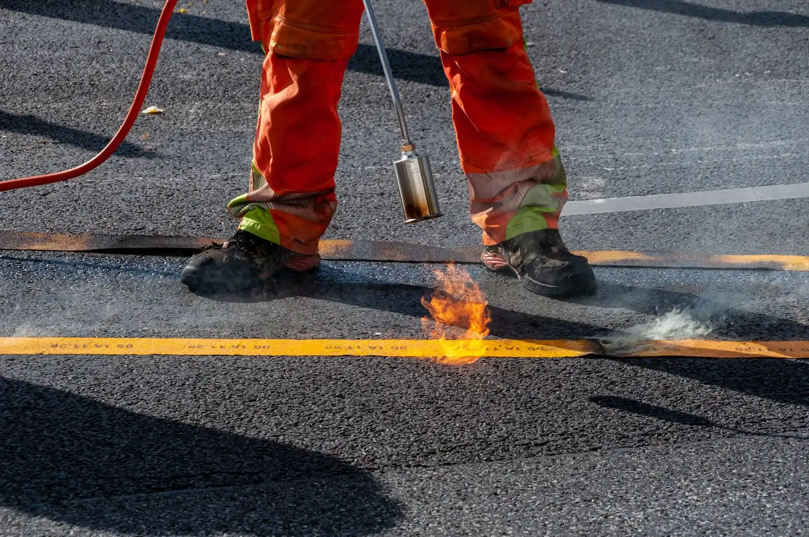 A worker sealing a pavement joint with a torch