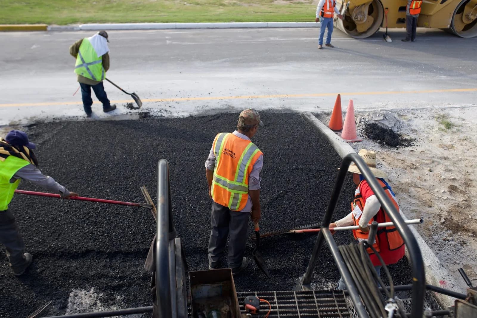Paving workers raking hot asphalt behind a paver
