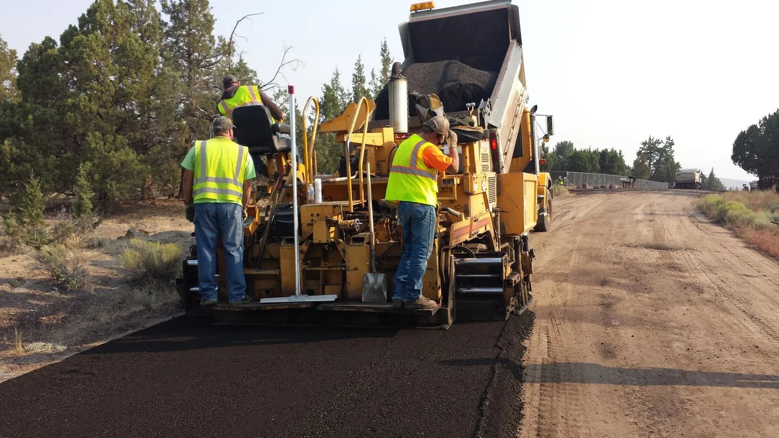 Two workers in high visibility clothing on an asphalt paver
