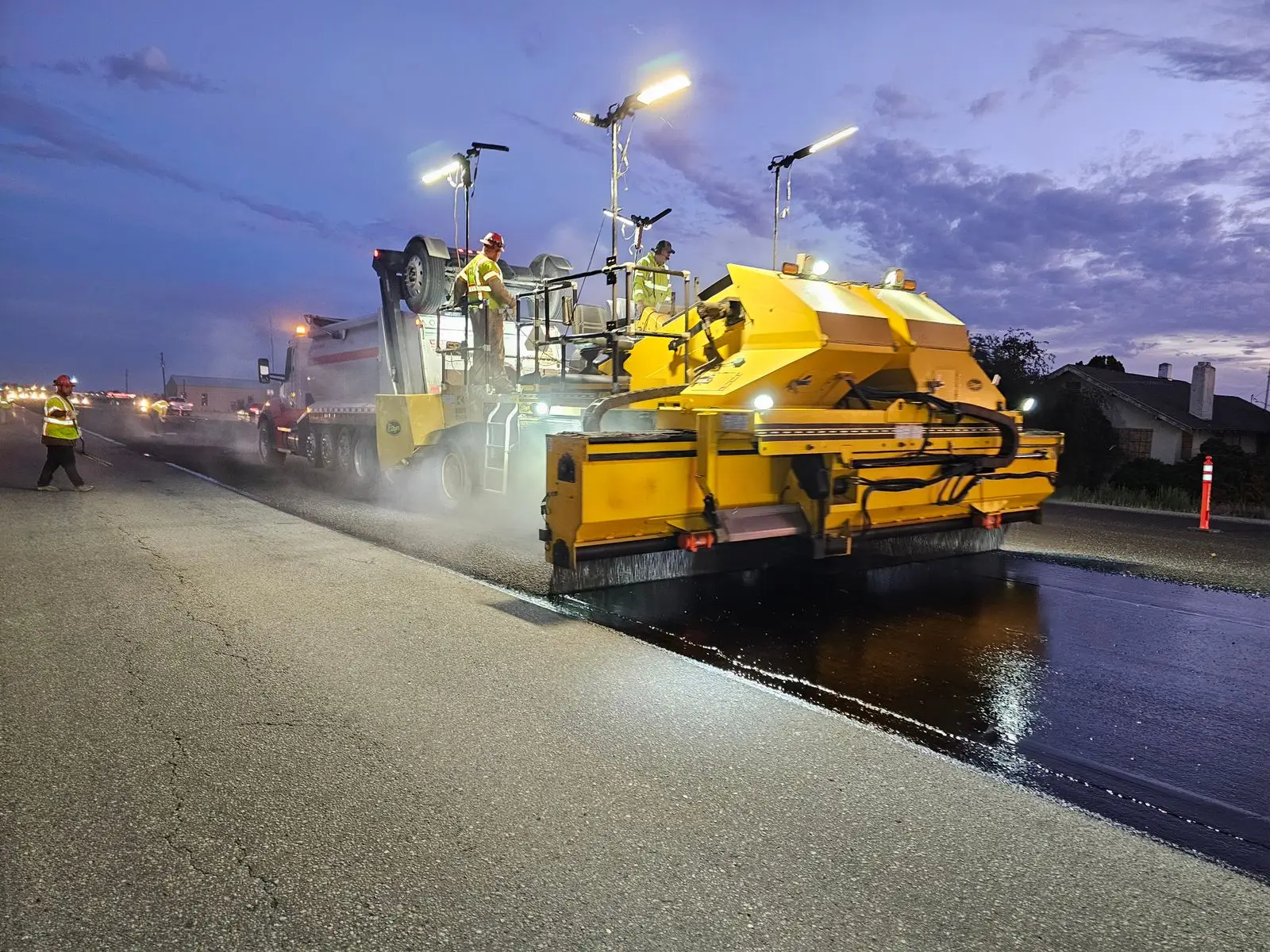 A yellow paver laying asphalt at dusk